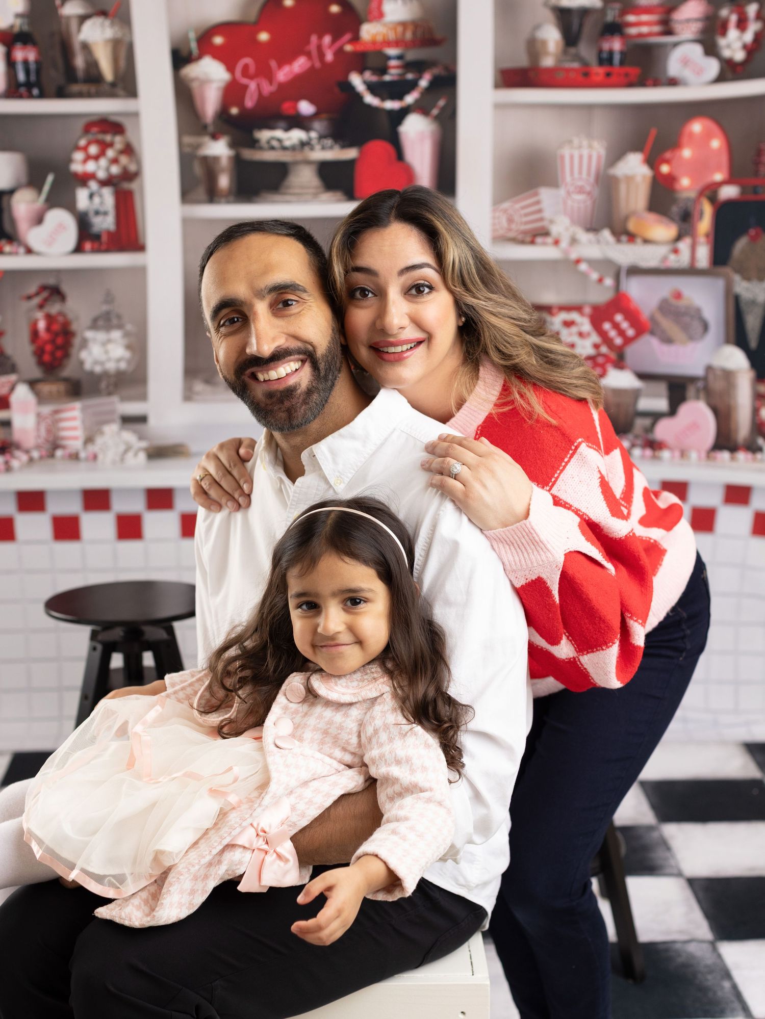 Family poses together in front of red and white retro diner-themed backdrop for holiday photos.