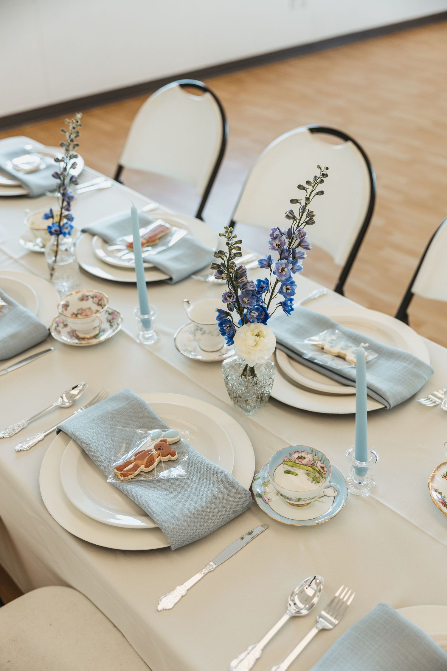 Elegant wedding table setting with blue candles, floral centerpieces, vintage china teacups, and light blue linen napkins.