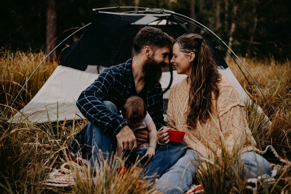 A couple sits together in tall grass during a romantic autumn photoshoot at sunset.