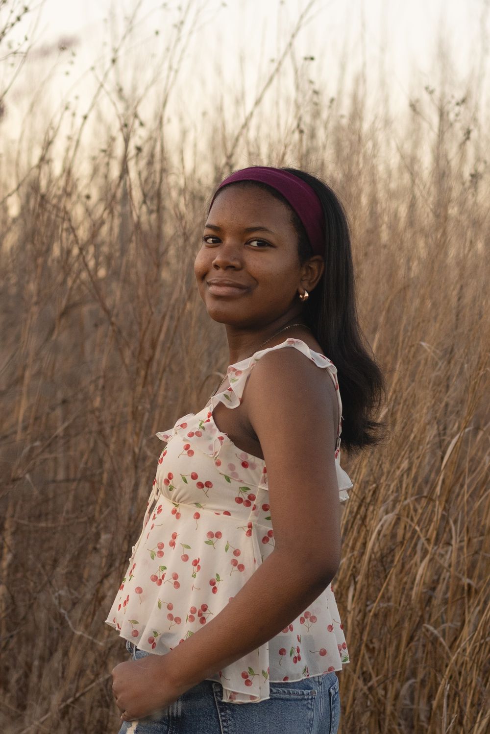 Candid portrait in a floral top and denim against golden dried grass.