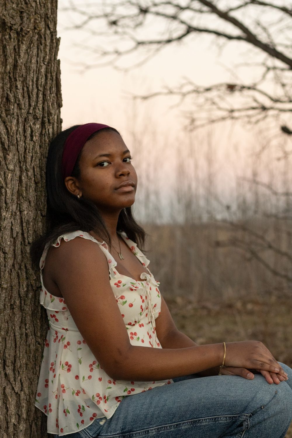 Thoughtful outdoor portrait leaning against a tree at dusk.