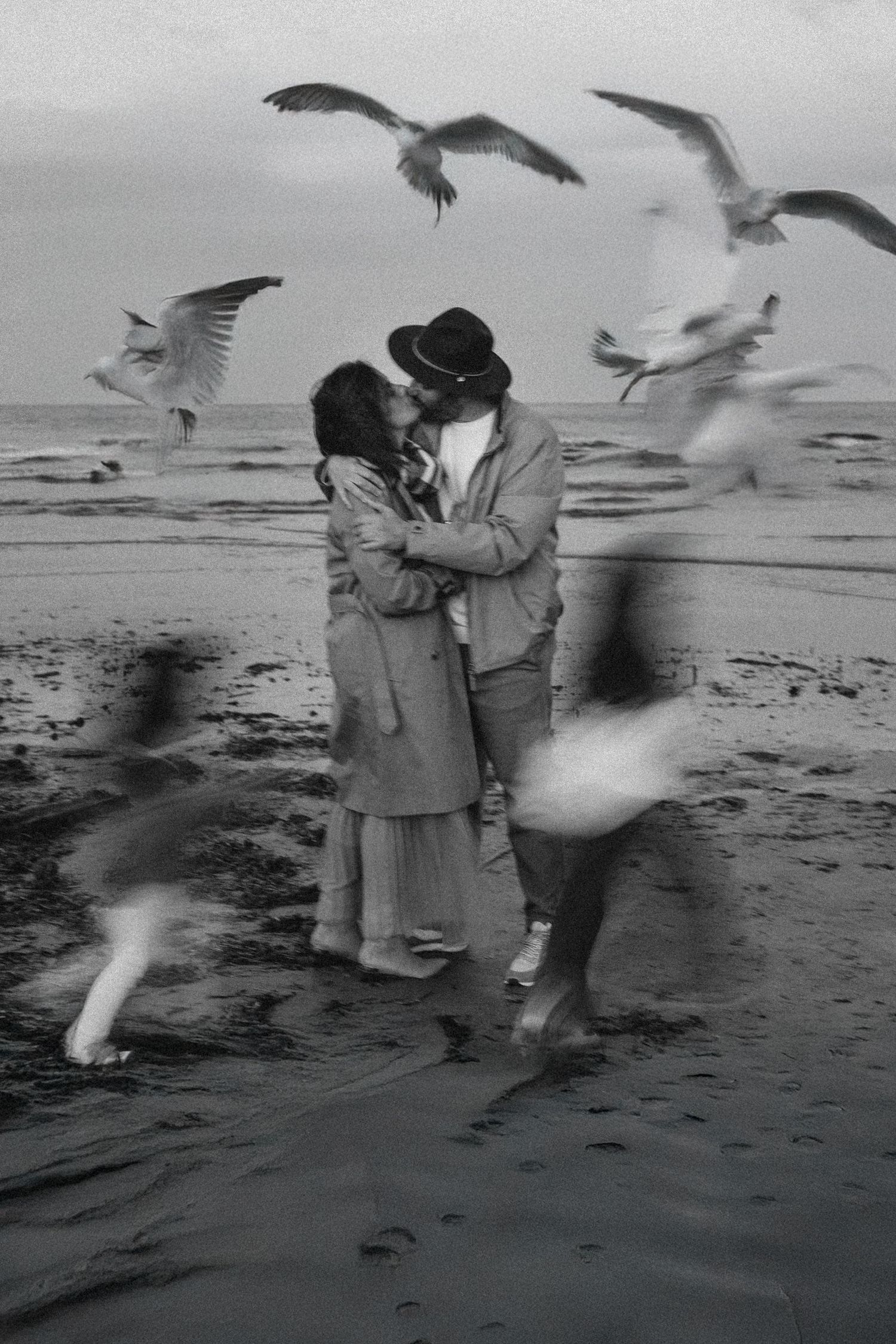 Vintage black and white photo sequence of people feeding seagulls on a beach as birds swoop down around them. Javea photographer