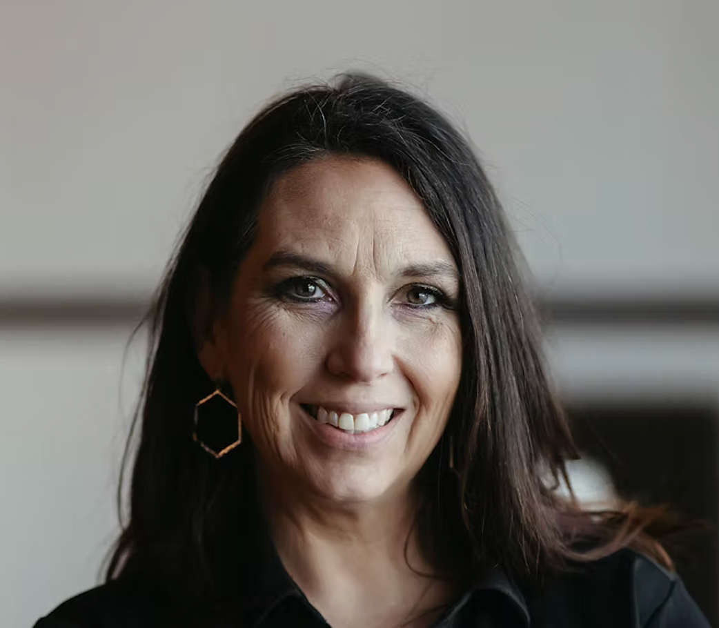 Portrait of a woman with long dark hair wearing a black top and hexagonal earrings.