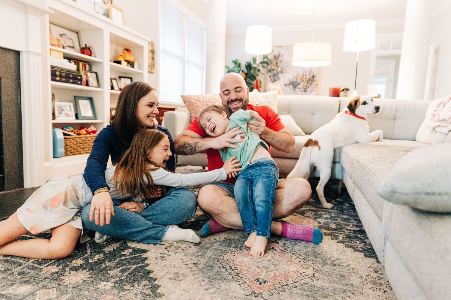 Family relaxes together on cozy living room floor with throw pillows and blankets during casual hangout at home.