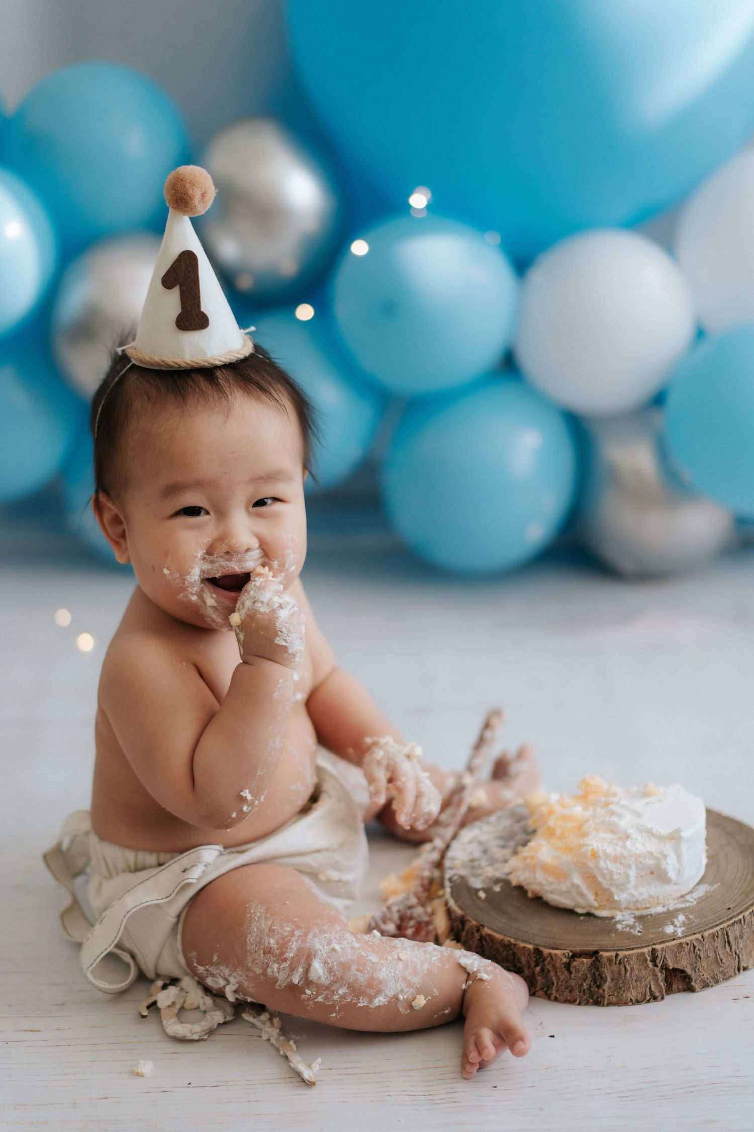 Baby's first birthday cake smash photo session with blue and white balloon backdrop and wooden cake stand.