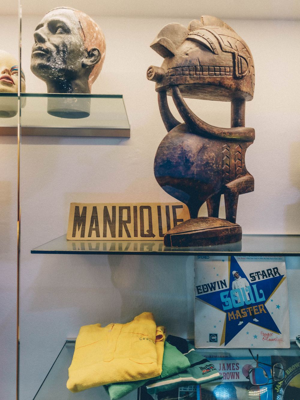 Display shelf with artistic sculptures, a helmet, and clothing items beneath a 'Manrique' sign in a retail setting.