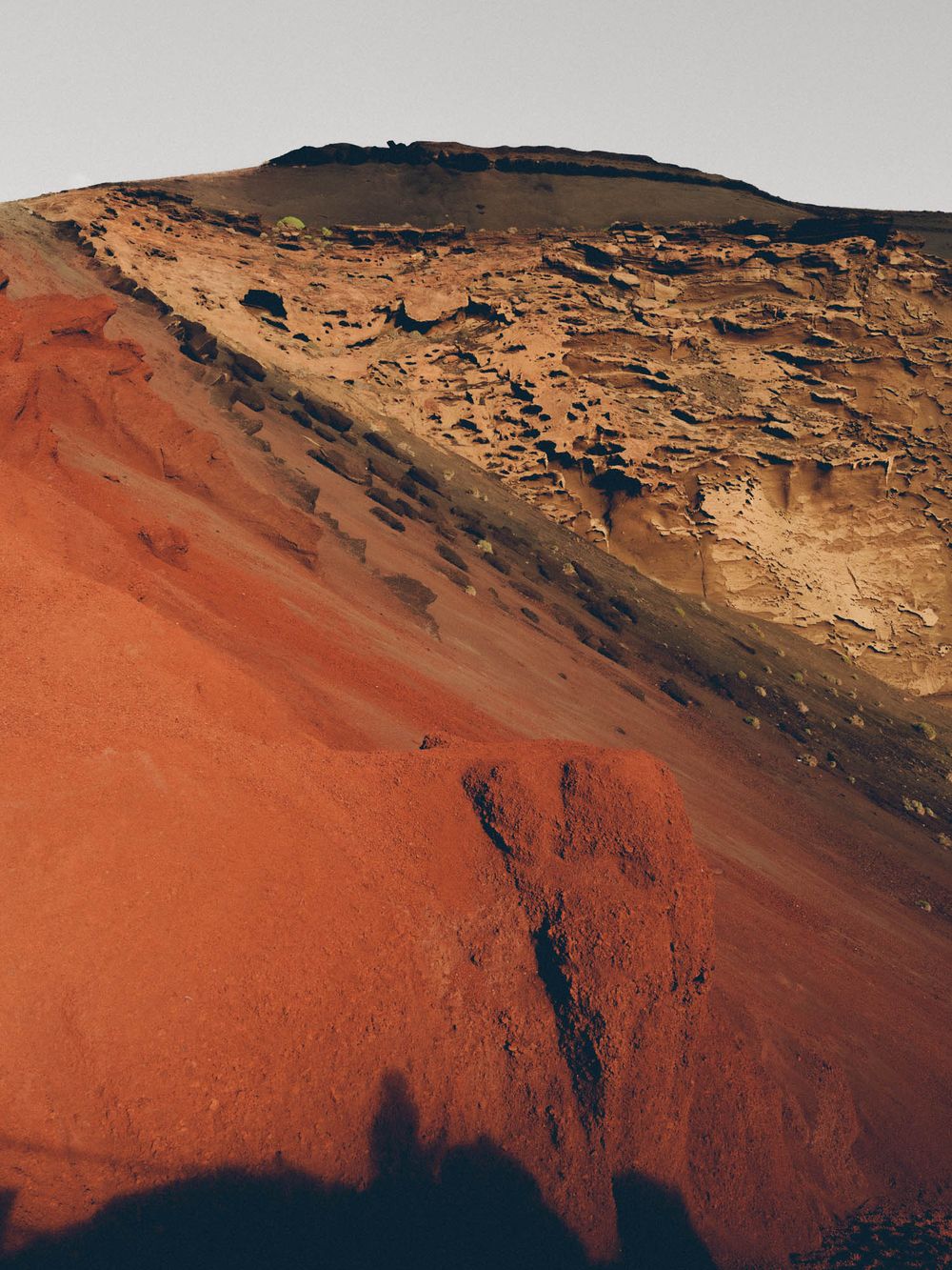 Dramatic aerial view of red and orange volcanic rock formations in a mountainous desert landscape at sunset.