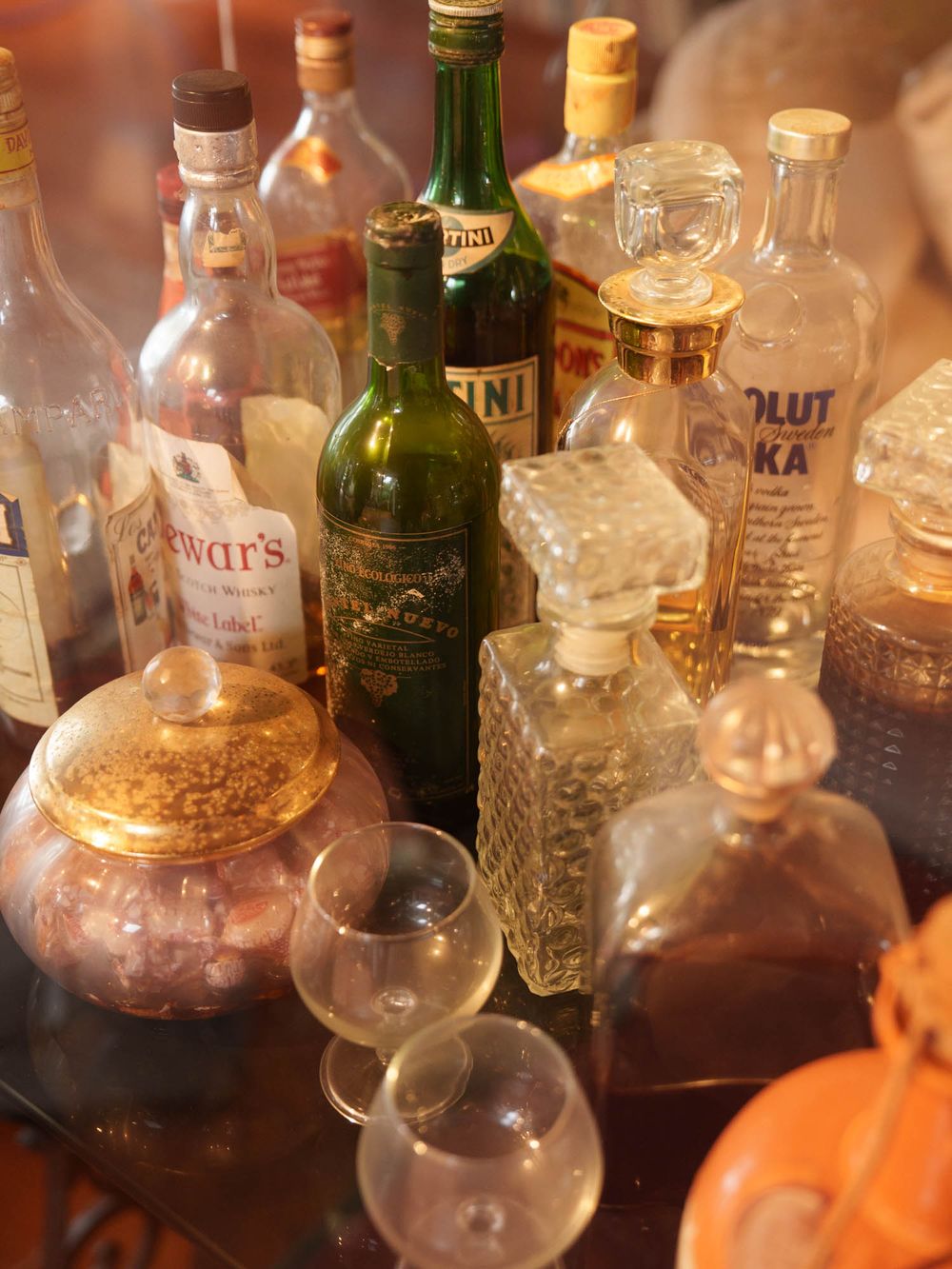 Collection of liquor bottles and glassware arranged on a table with warm ambient lighting.