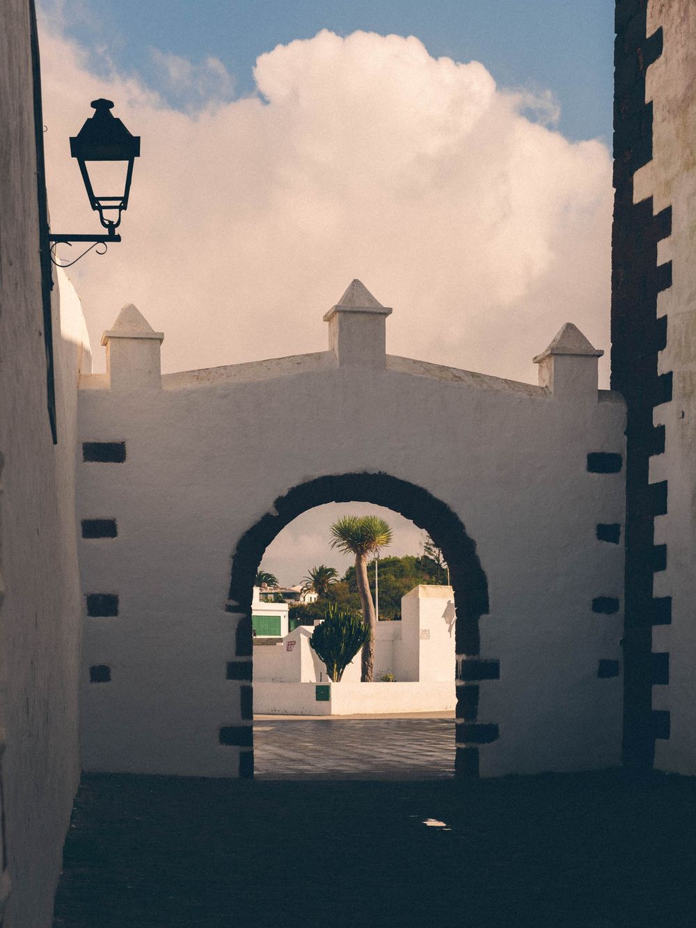 White stone archways and columns frame a scenic view of a traditional Spanish colonial style building under cloudy skies.