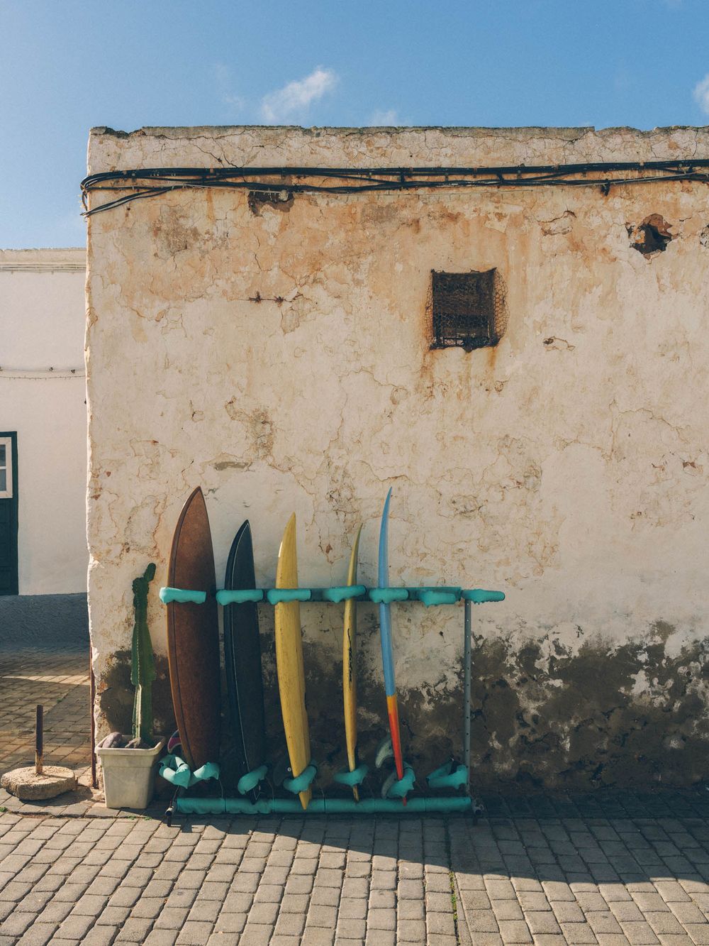 A row of surfboards leaning against a weathered beige wall with shadows cast in the sunlight.