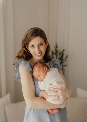 A tender moment captured as a mother in a light blue dress holds and gazes lovingly at her sleeping newborn baby.