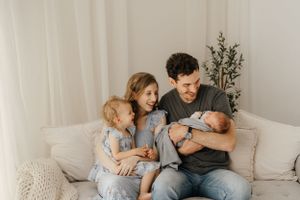 A family relaxes together on a white couch in a bright, minimalist living room with light decor.