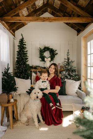 A cozy Christmas scene with white walls, artificial trees, and a large white dog sitting on a plush couch in a rustic room.