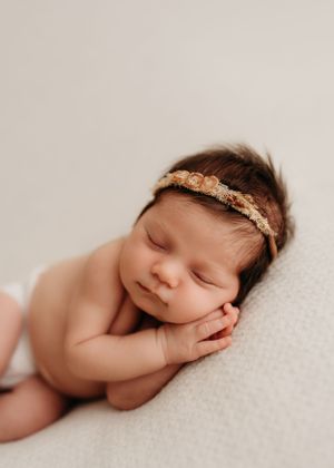 Peaceful sleeping newborn baby wearing delicate lace headband rests on soft white blanket in natural light.