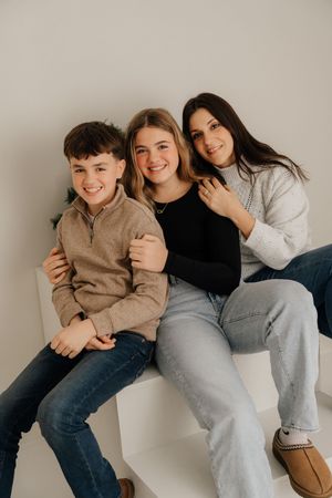 Group of friends in casual clothing sitting and laughing together against a white wall in a candid photo series.