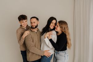 Friends in jeans and sweaters posing playfully against white wall in casual indoor photoshoot.