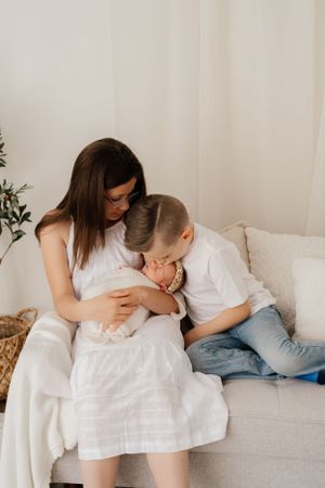 A tender moment shared on a light gray couch as parents cuddle with their newborn baby in a bright, minimalist setting.