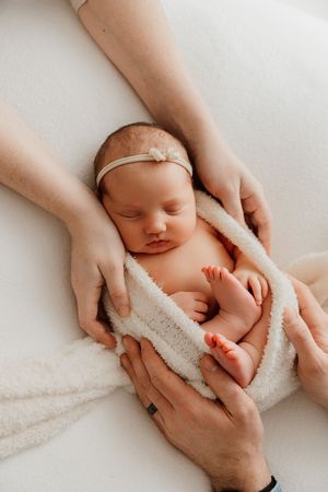A series of tender newborn photography shots showing gentle hands cradling a sleeping baby wrapped in soft white fabric.