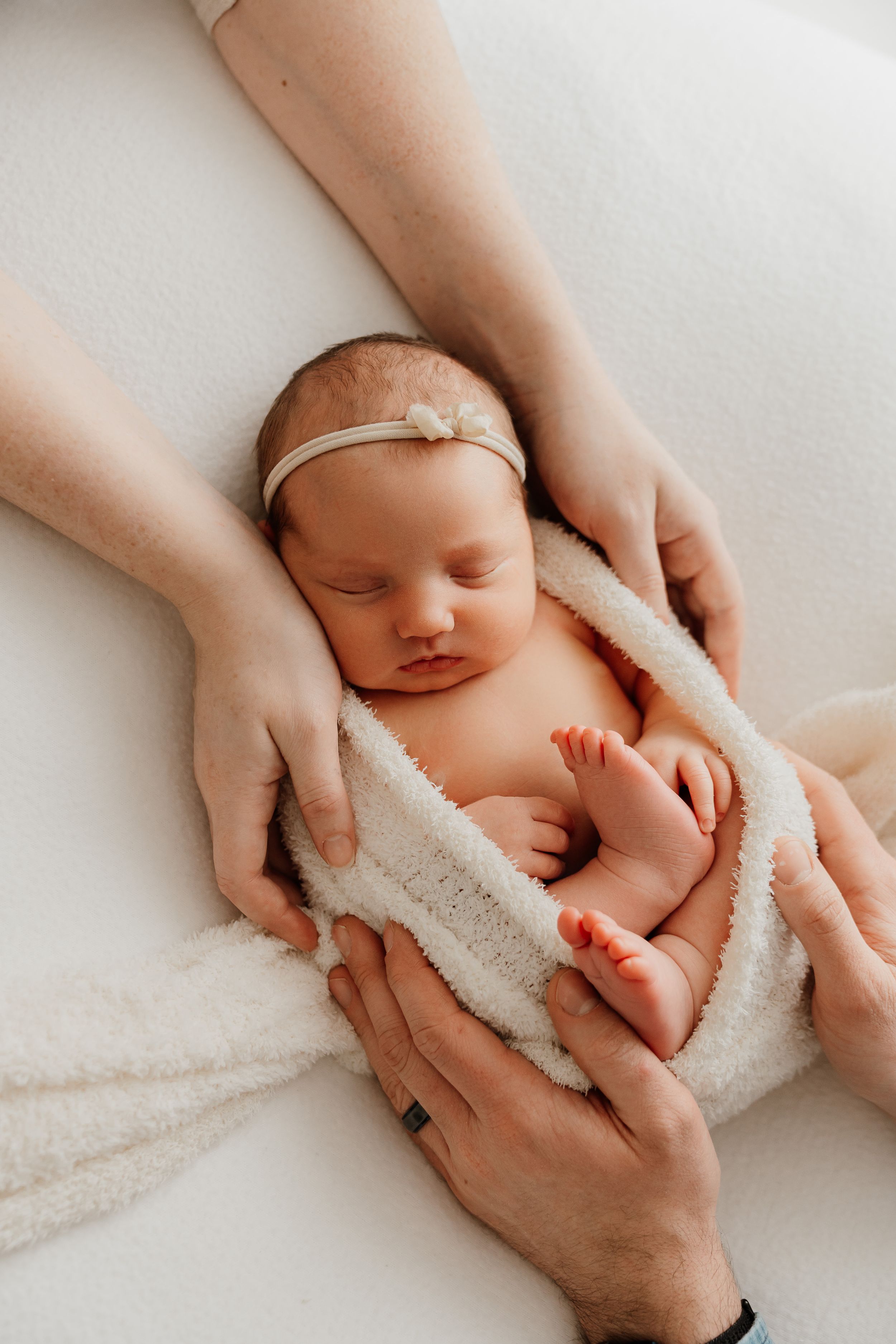 A series of tender newborn photography shots showing gentle hands cradling a sleeping baby wrapped in soft white fabric.