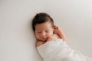 Peacefully sleeping newborn swaddled in soft white fabric against white background with content expression.