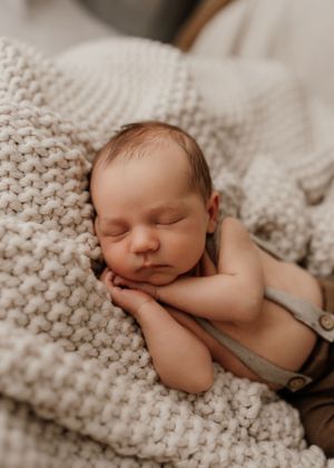 Peaceful sleeping newborn on chunky knit blanket in natural light.