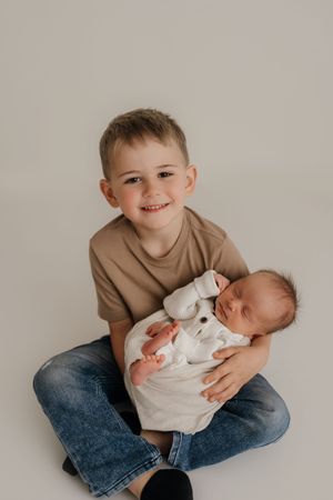 Two children pose in casual clothing on a white studio backdrop in a sweet family portrait series.