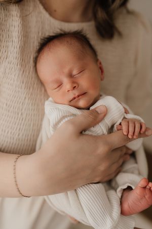 Gentle close-up shots of a sleeping newborn swaddled in white fabric being cradled by caring hands.