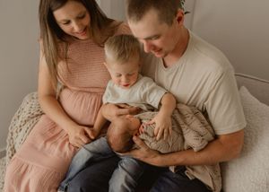 Family in muted tones sits together on cozy seat while looking at mobile device.