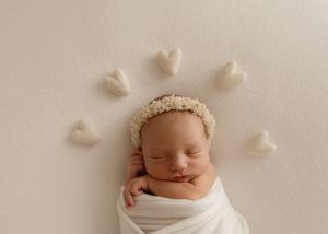 A sleeping newborn wrapped in white fabric with decorative heart shapes arranged above their head.