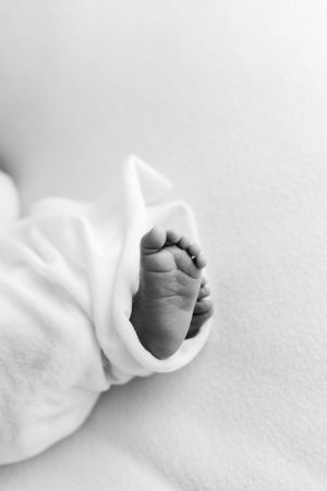 Close-up black and white photograph of a tiny baby foot wrapped in soft white blanket.