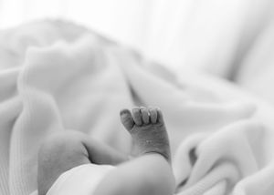 A tiny baby foot rests against soft white bedding in a tender black and white photograph.