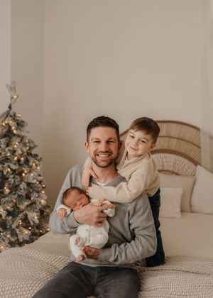A heartwarming family moment in front of a decorated Christmas tree on a cozy bed with rattan headboard.