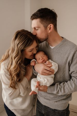 Tender family moment with new parents cradling sleeping newborn.