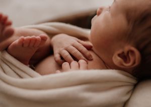 Close-up view of a sleeping baby's hands and feet wrapped in soft beige blanket.