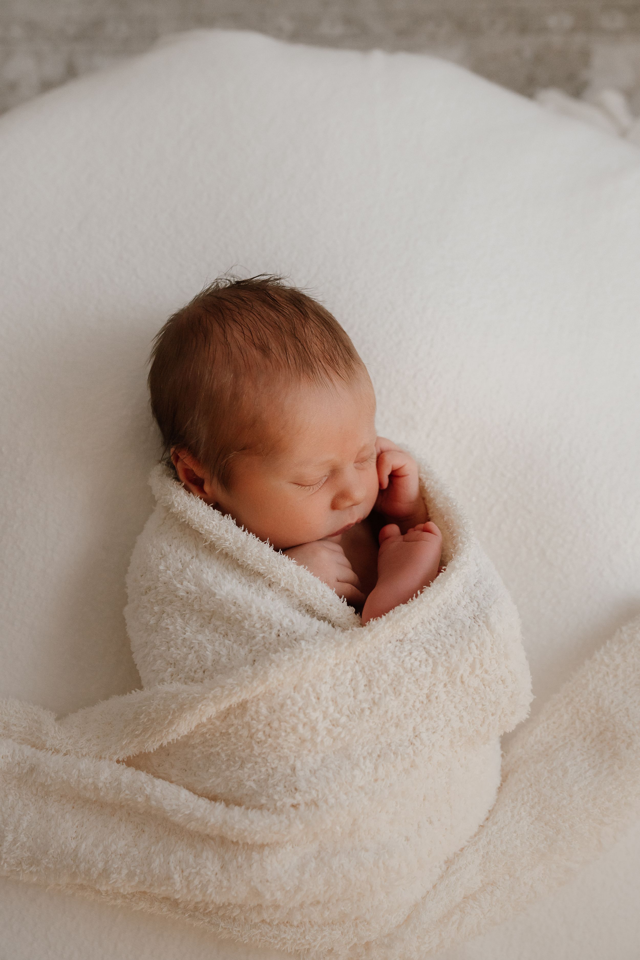 A sleeping newborn baby wrapped in soft white blankets shown in a series of gentle, peaceful poses.