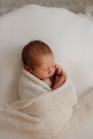 A sleeping newborn baby wrapped in soft white blankets shown in a series of gentle, peaceful poses.