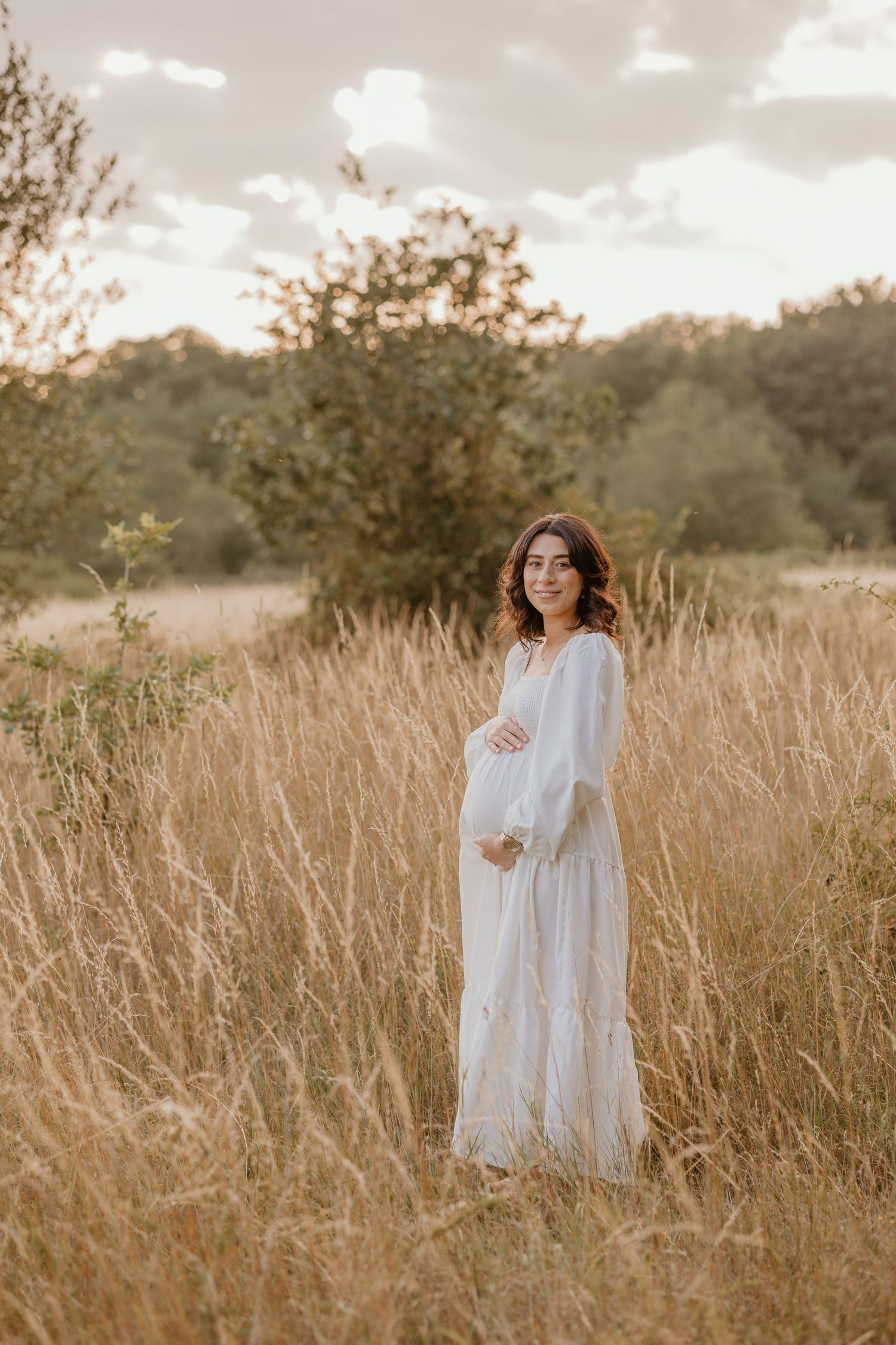 Woman in flowing white dress twirling through golden sunlit field during sunset.