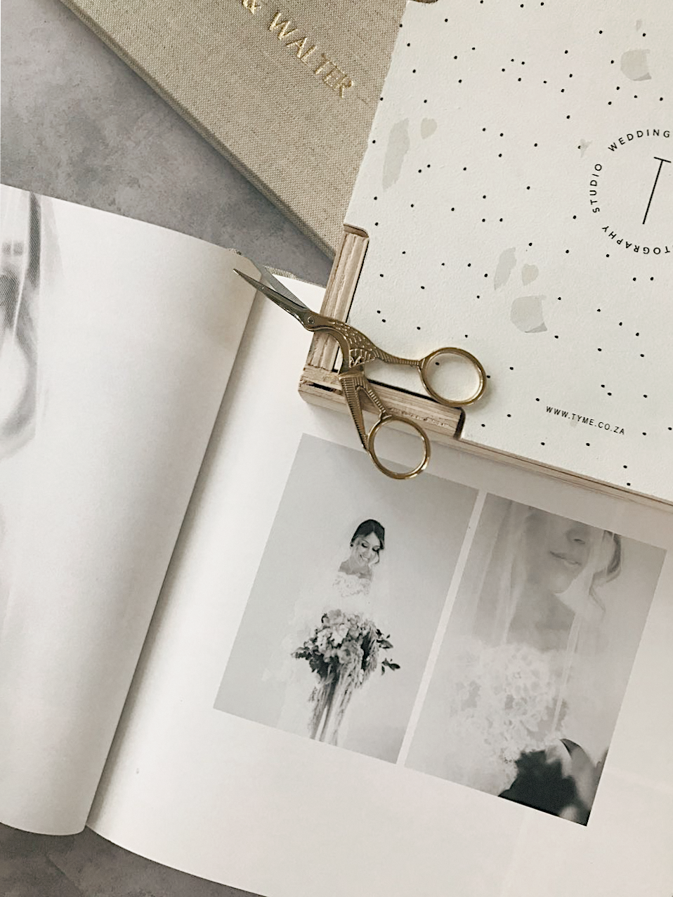 Open wedding photography book with gold scissors resting on dotted studio branding guide on marble surface.
