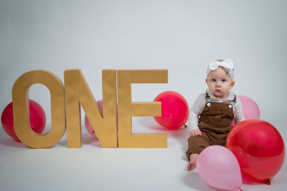 A series of images showing gold 'ONE' letters with pink and brown balloons for a first birthday celebration.