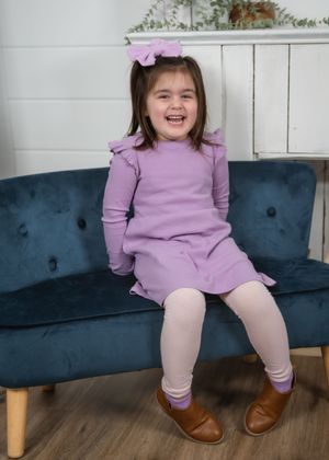 A child in a purple sweater and pink tights sits on a navy blue tufted bench with wooden legs.