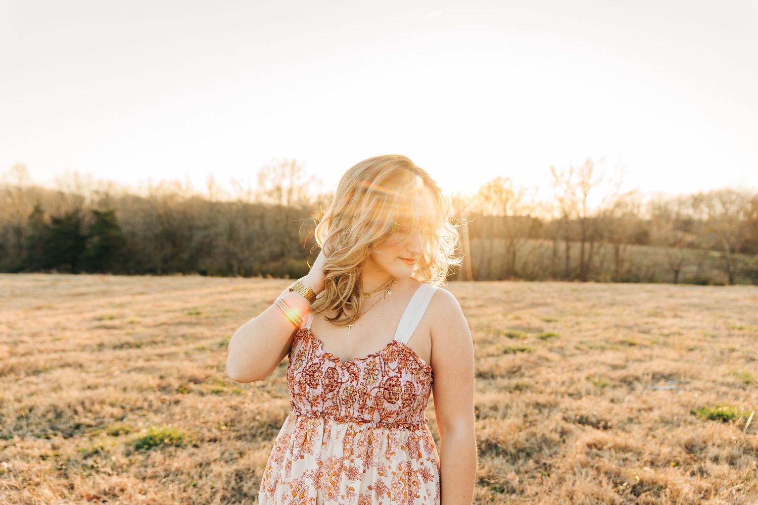 A person in a floral dress stands in a golden field at sunset with warm glowing light for branding photos.