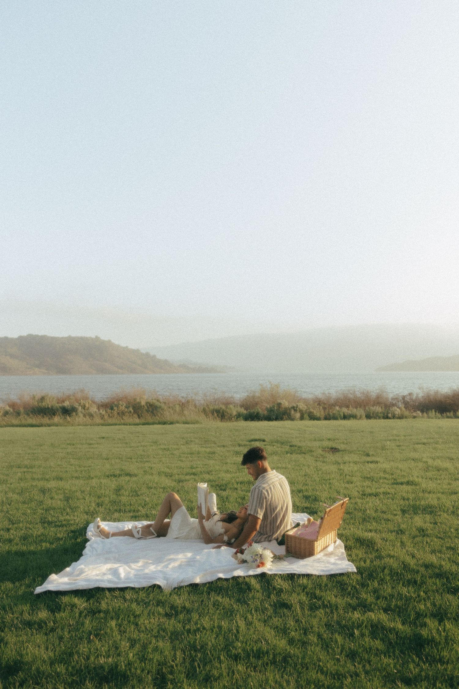 Person enjoying a scenic picnic on a blanket overlooking a misty lake and rolling hills on a peaceful afternoon.