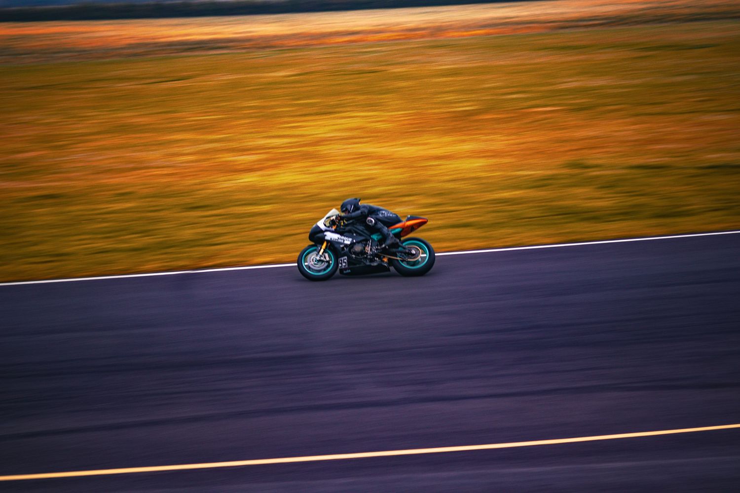 A motorcycle rider leans into a turn on a racetrack during sunset with motion blur in the background.