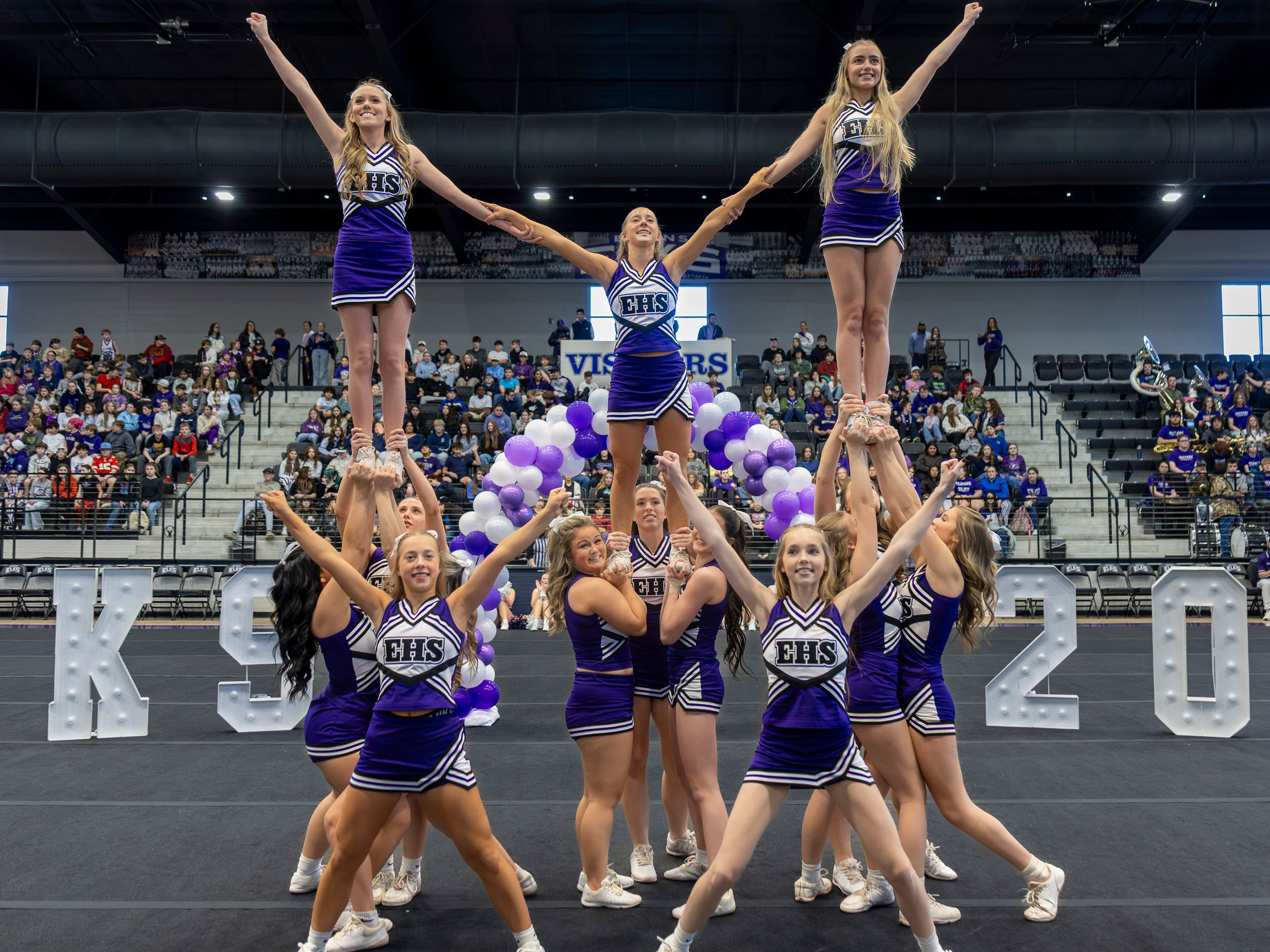 Cheerleaders in purple uniforms perform synchronized stunts and formations during a sports event.