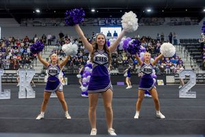 Cheerleaders in purple and white uniforms perform synchronized dance moves during a sports event.