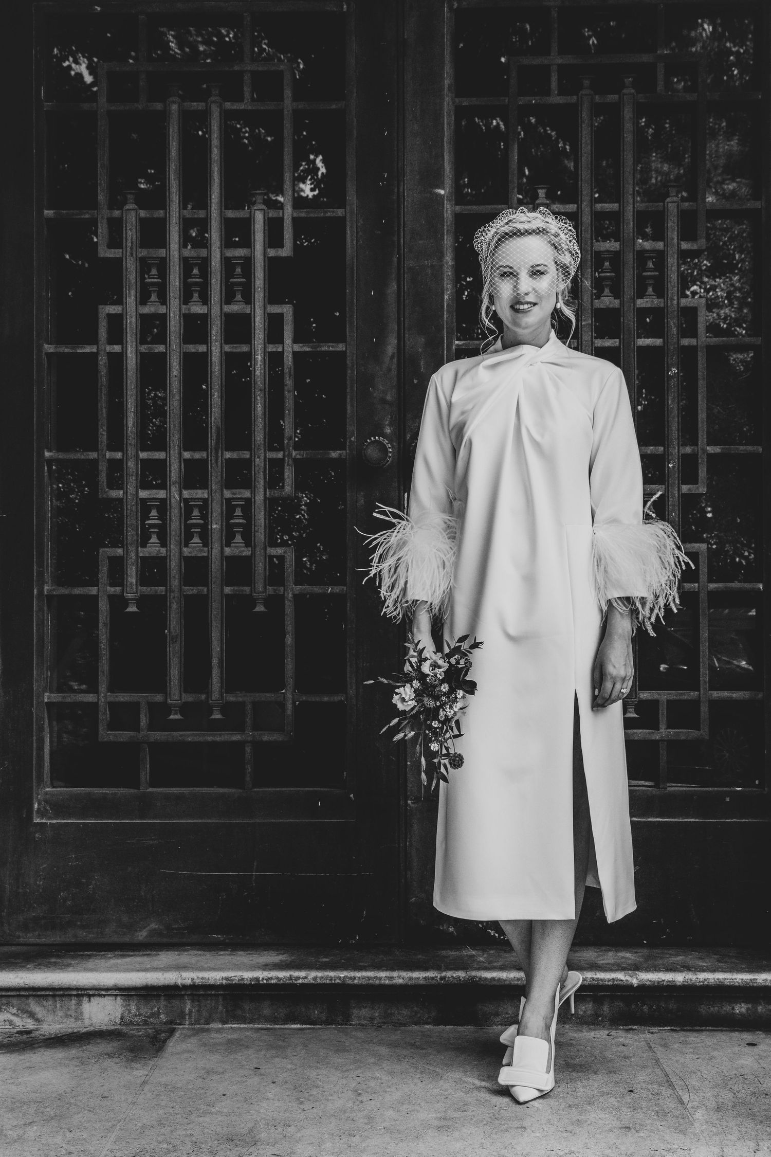 A vintage-style black and white photo showing a bride in a white dress standing against a dark patterned wall, at Stoke Newington Town hall