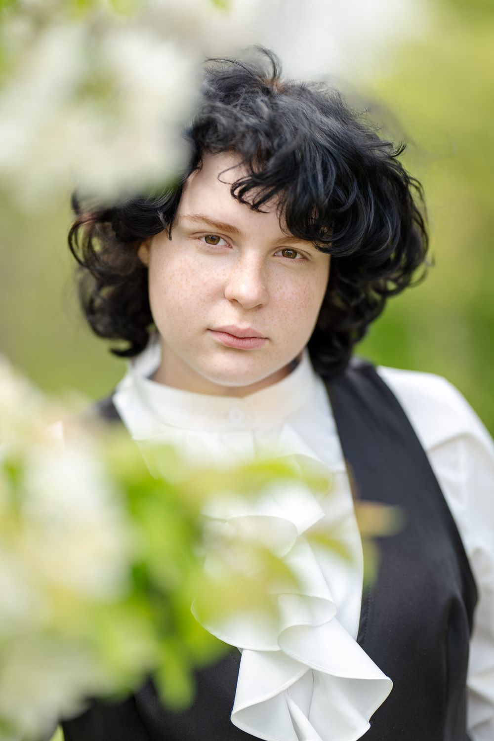 Portrait against blurred green foliage background wearing black vest and white ruffled collar.