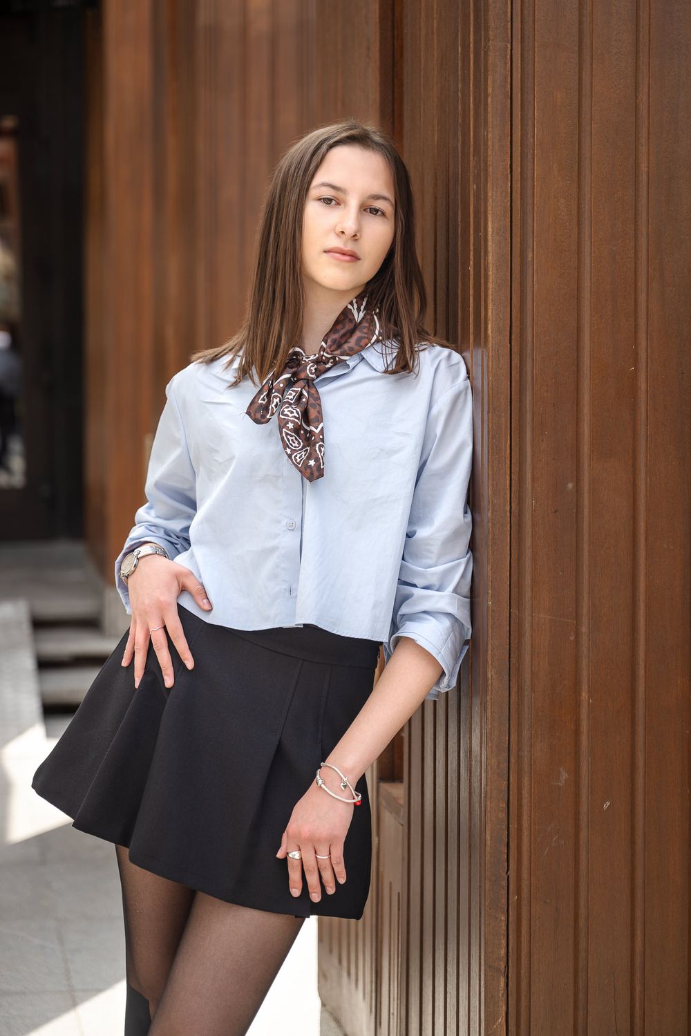 A series of fashion photos showing a person in a light blue button-up shirt and black pleated skirt against wooden panels.