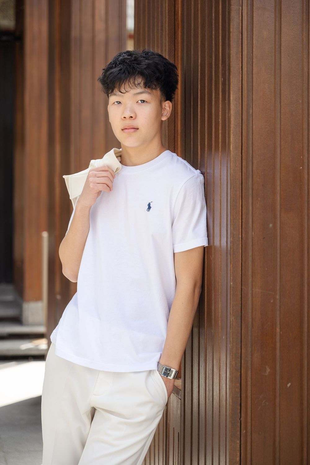Person in white t-shirt and beige pants poses against wooden paneled wall in multiple casual stances.