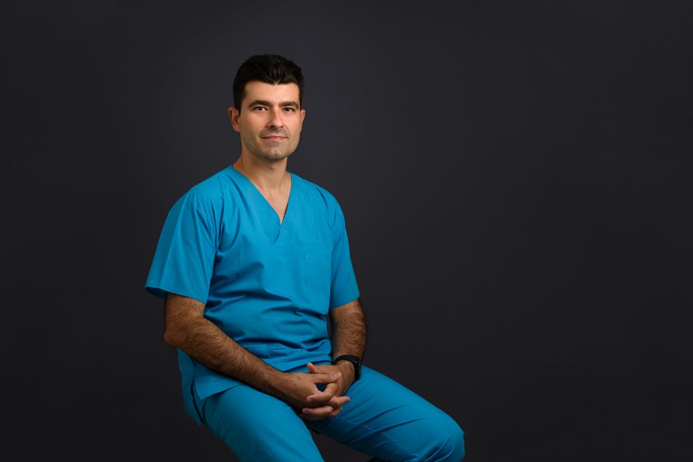 Healthcare professional in blue scrubs seated against dark background.